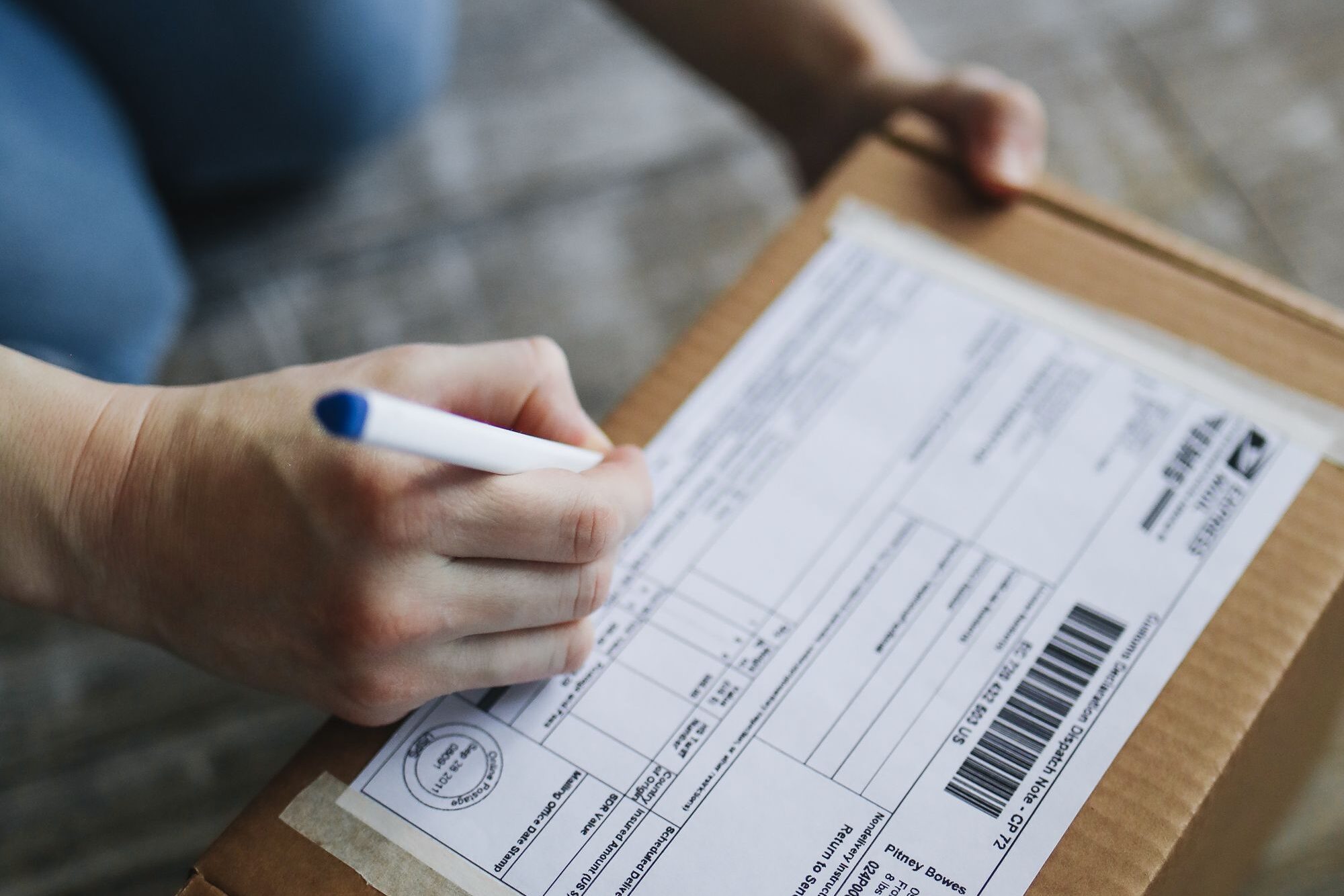 Close-up view of hands writing on a shipping box indoors.