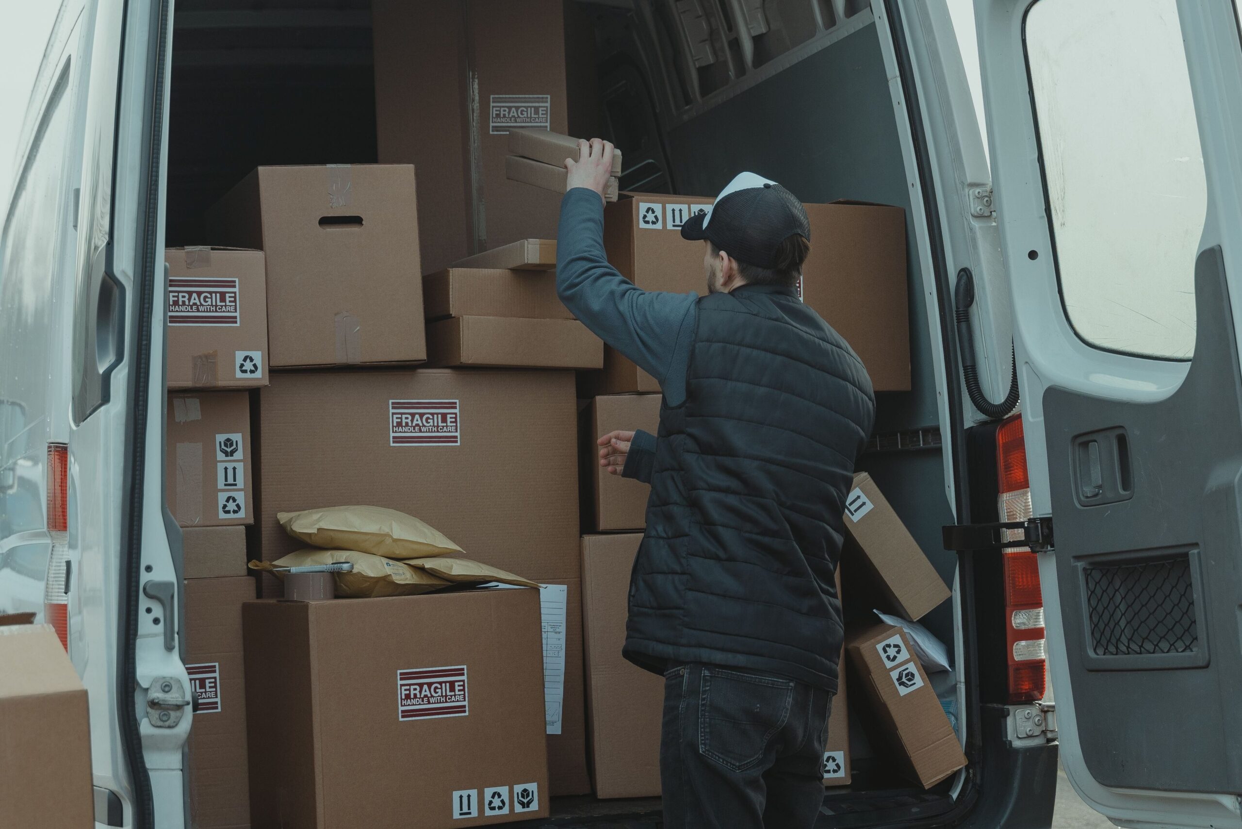 A courier organizing boxes in a delivery van for shipment on a cloudy day.
