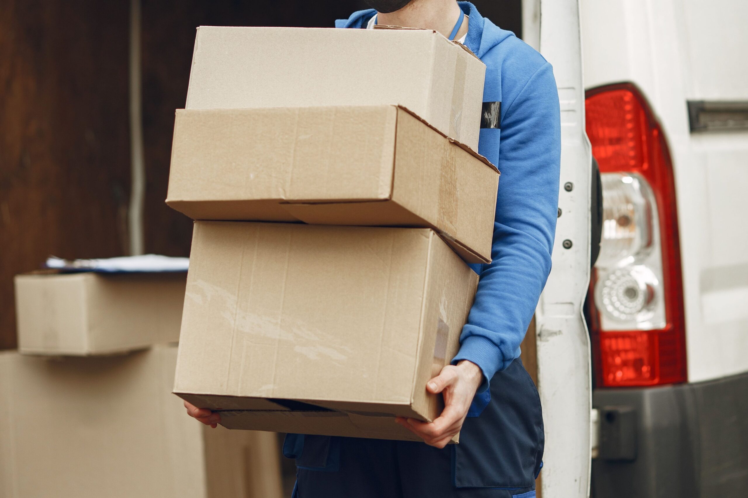 Man wearing mask delivering cardboard boxes from van outdoors.